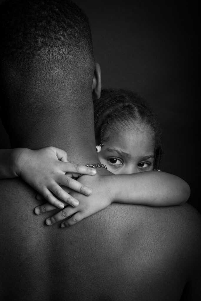 mamad, photo studio noir et blanc, torse nu, soeur, petite fille dans les bras regard intense, jeune homme noir - série de photo portait réalisée par Anael Jourdain Photographe Amateur Hauts-de-France